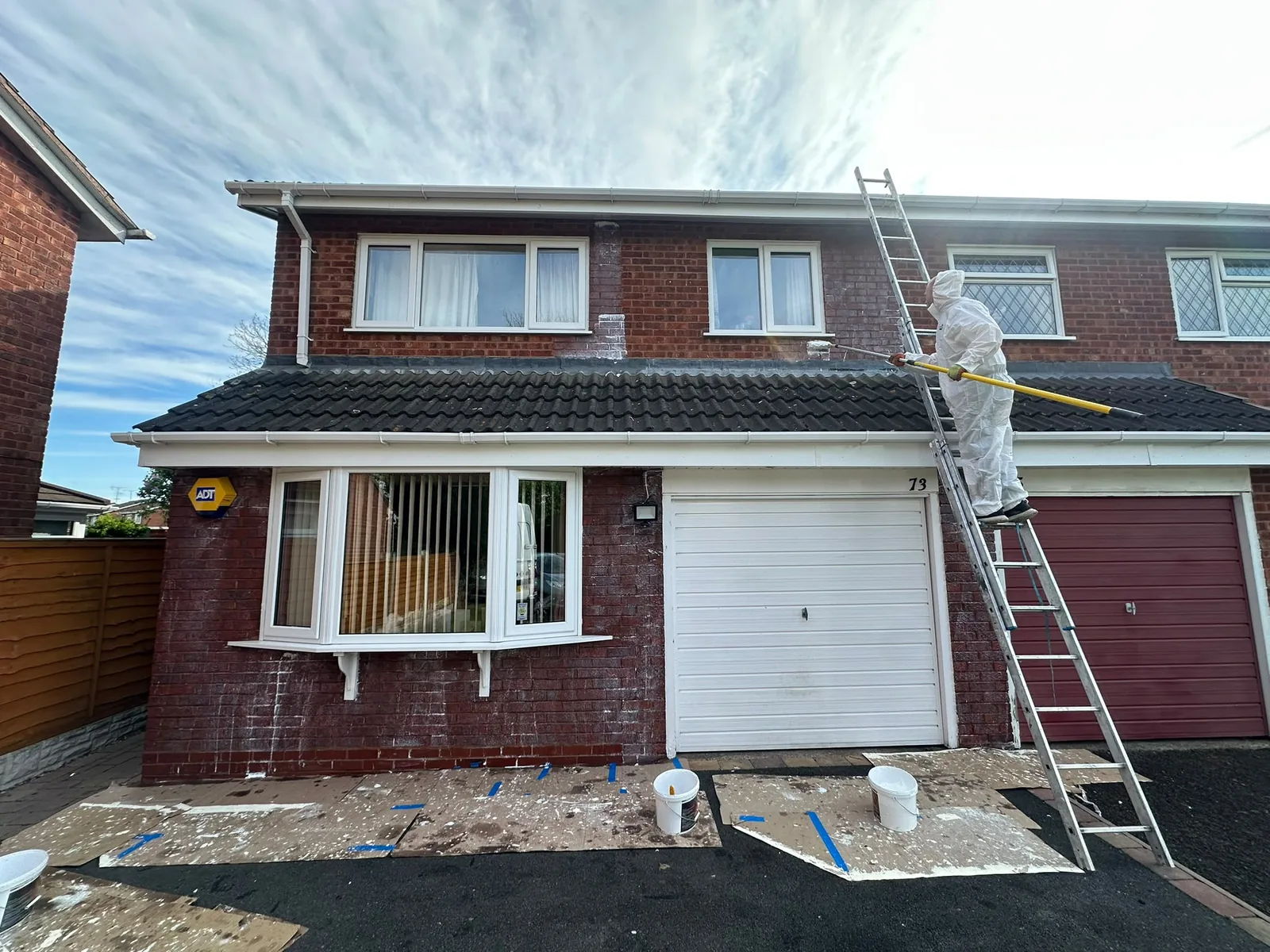 Apex worker on a ladder treating the rendered wall of a house