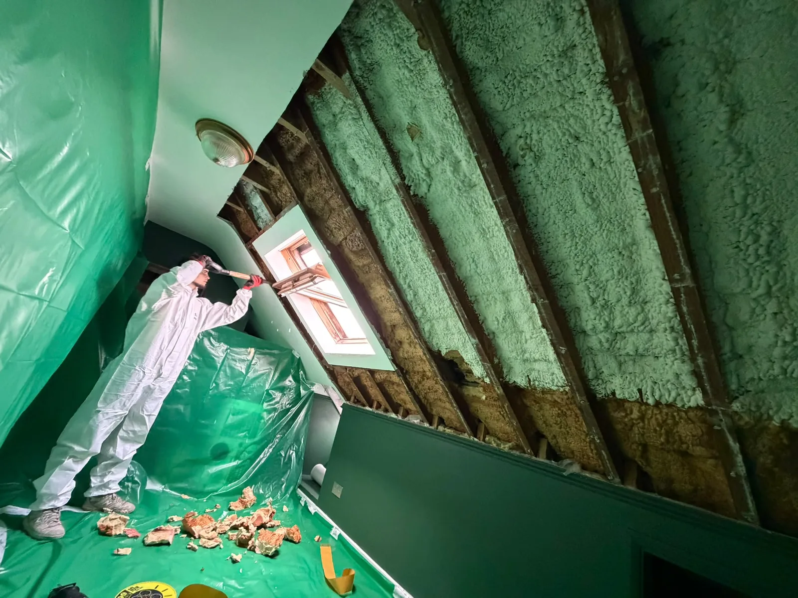 Technician removing spray foam beside a roof window in a sheeted loft